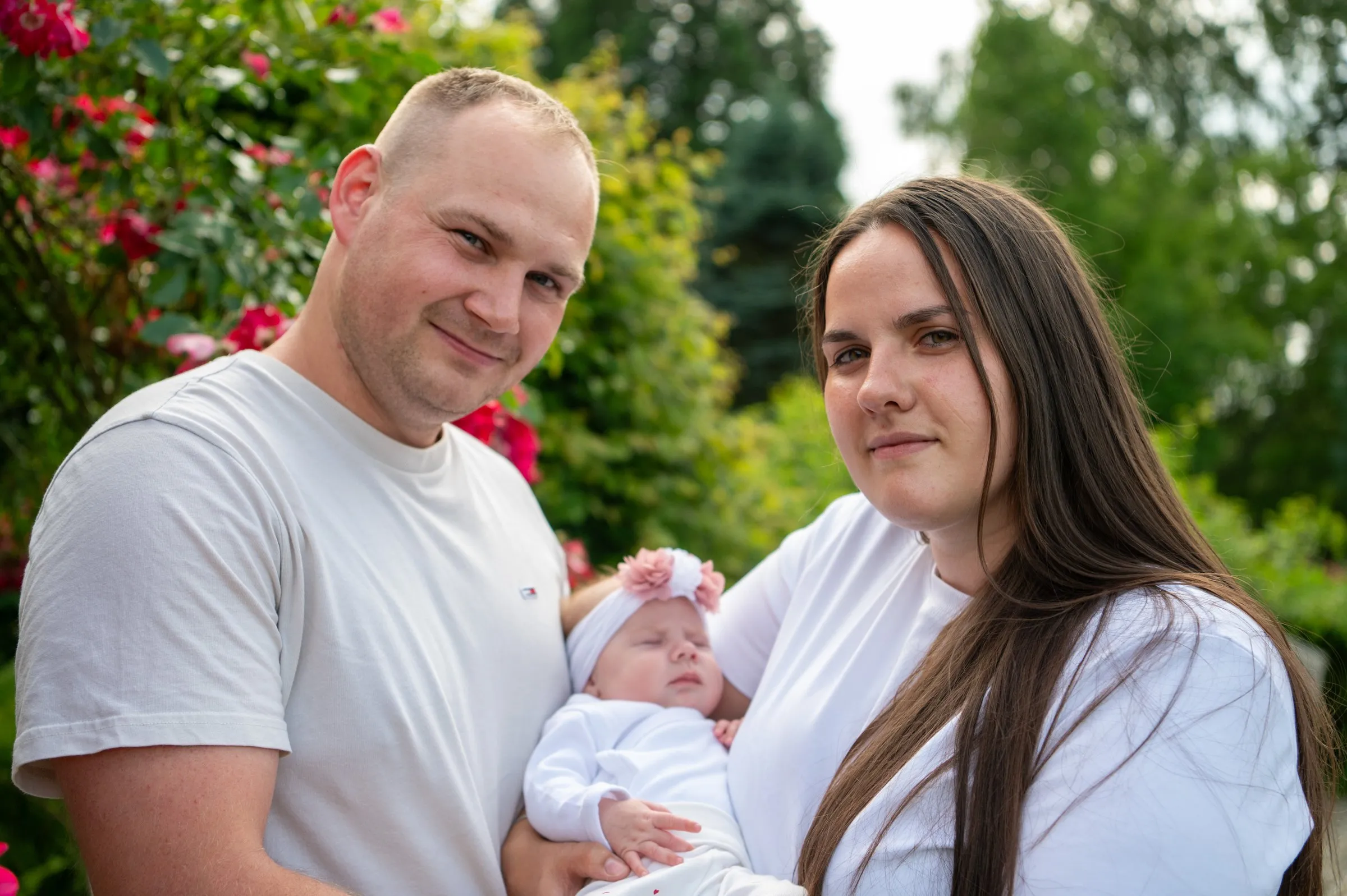 Rodzice z niemowlęciem przy krzewach róż